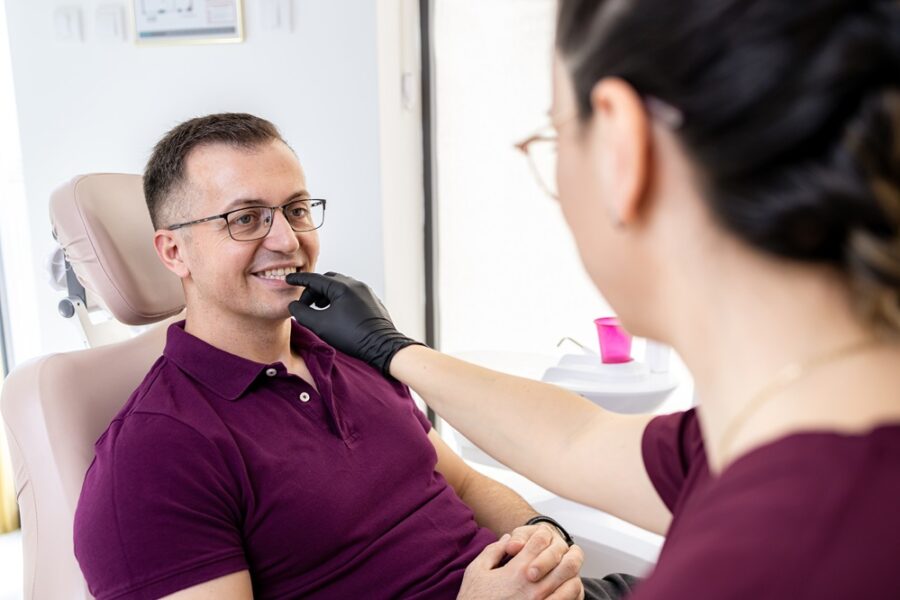 Smiling man in glasses in a dental chair as a dental team member gently checks his teeth during a veneers visit in Woodbridge, VA