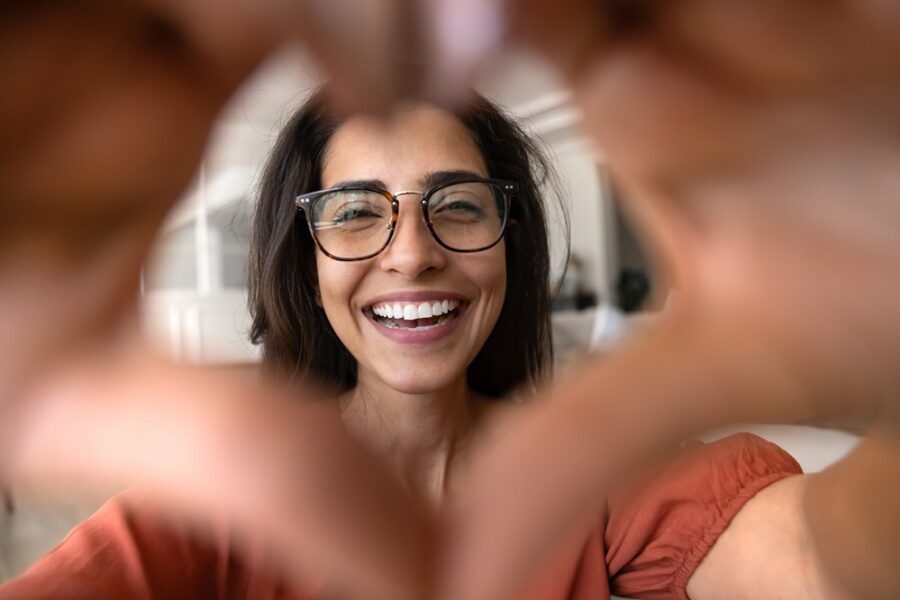 Smiling woman in glasses framing her face with her hands in a heart shape, showing the confidence of a smile makeover in Woodbridge, VA