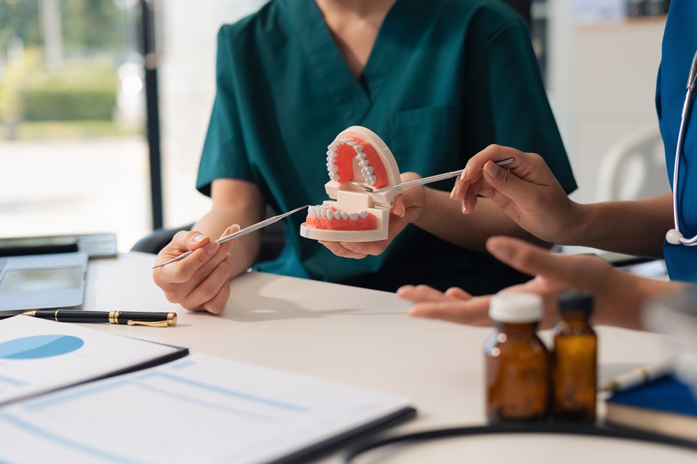 Dental team members in scrubs pointing to a tooth model while discussing restorative dentistry options in Woodbridge, VA 