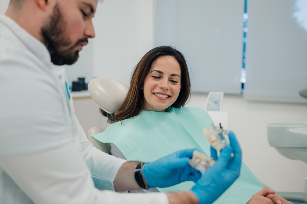Dentist in blue gloves showing a dental model to a smiling patient in the chair during a restorative care visit in Woodbridge, VA 